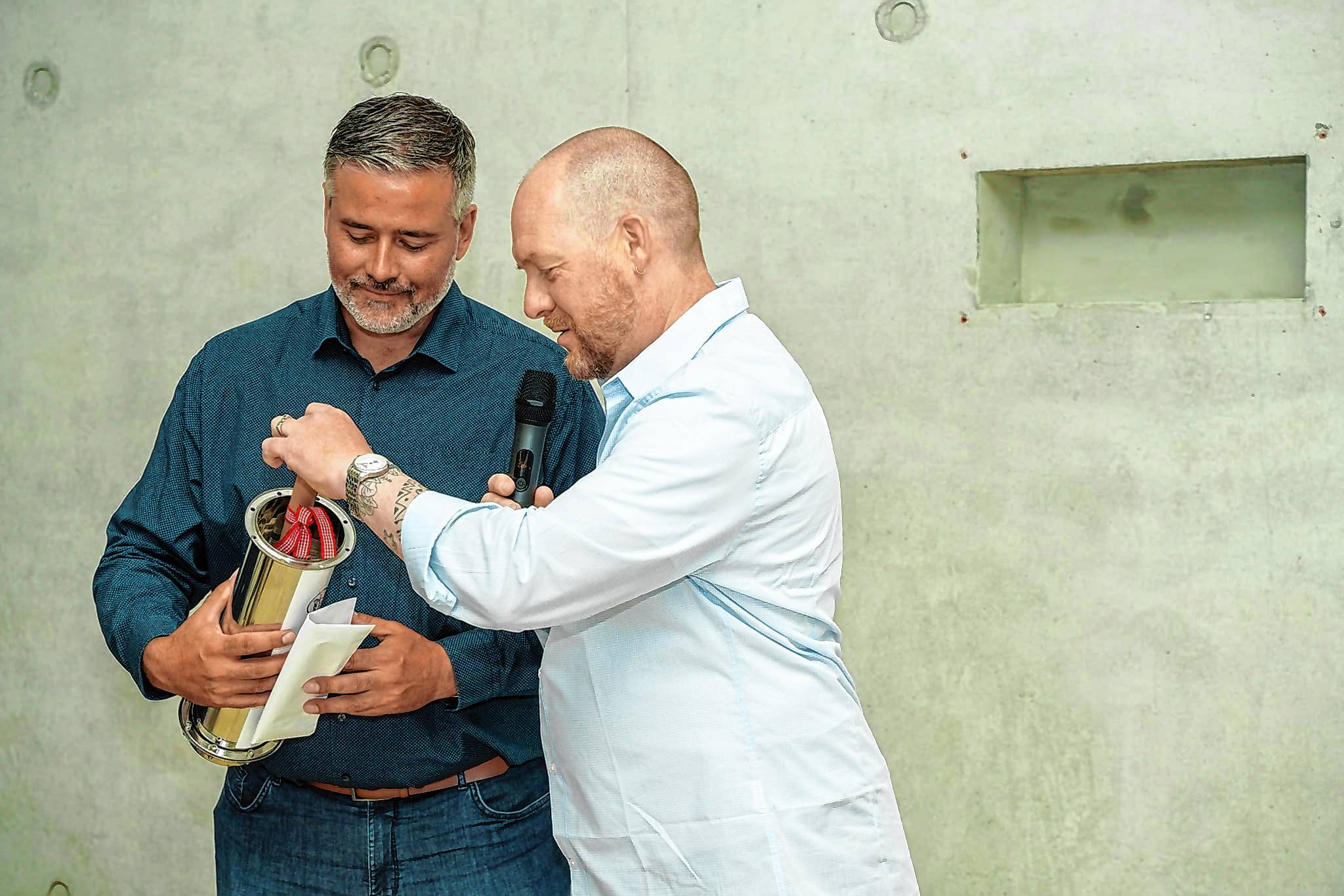 Die Schulleiter Jörg Gerspach (links) und Felix Bubner befüllen die Zeitkapsel, die in eine Wandnische eigebaut wird.