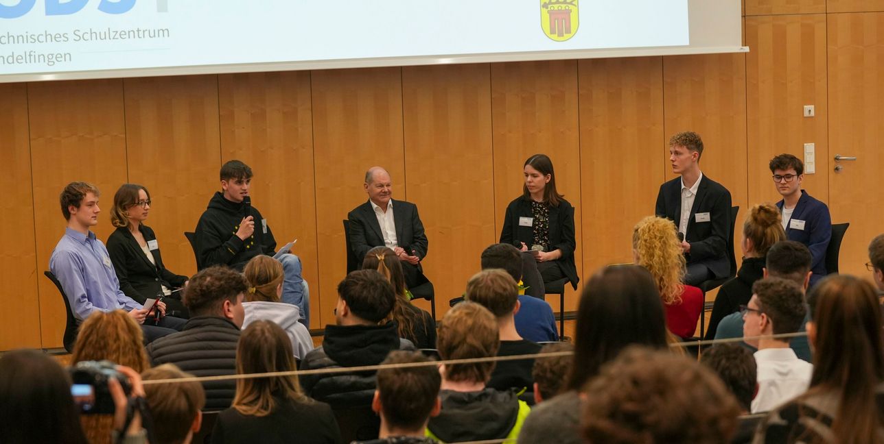 Der Kanzler steht den Schülern bei einer Podiumsdiskussion Rede und Antwort.