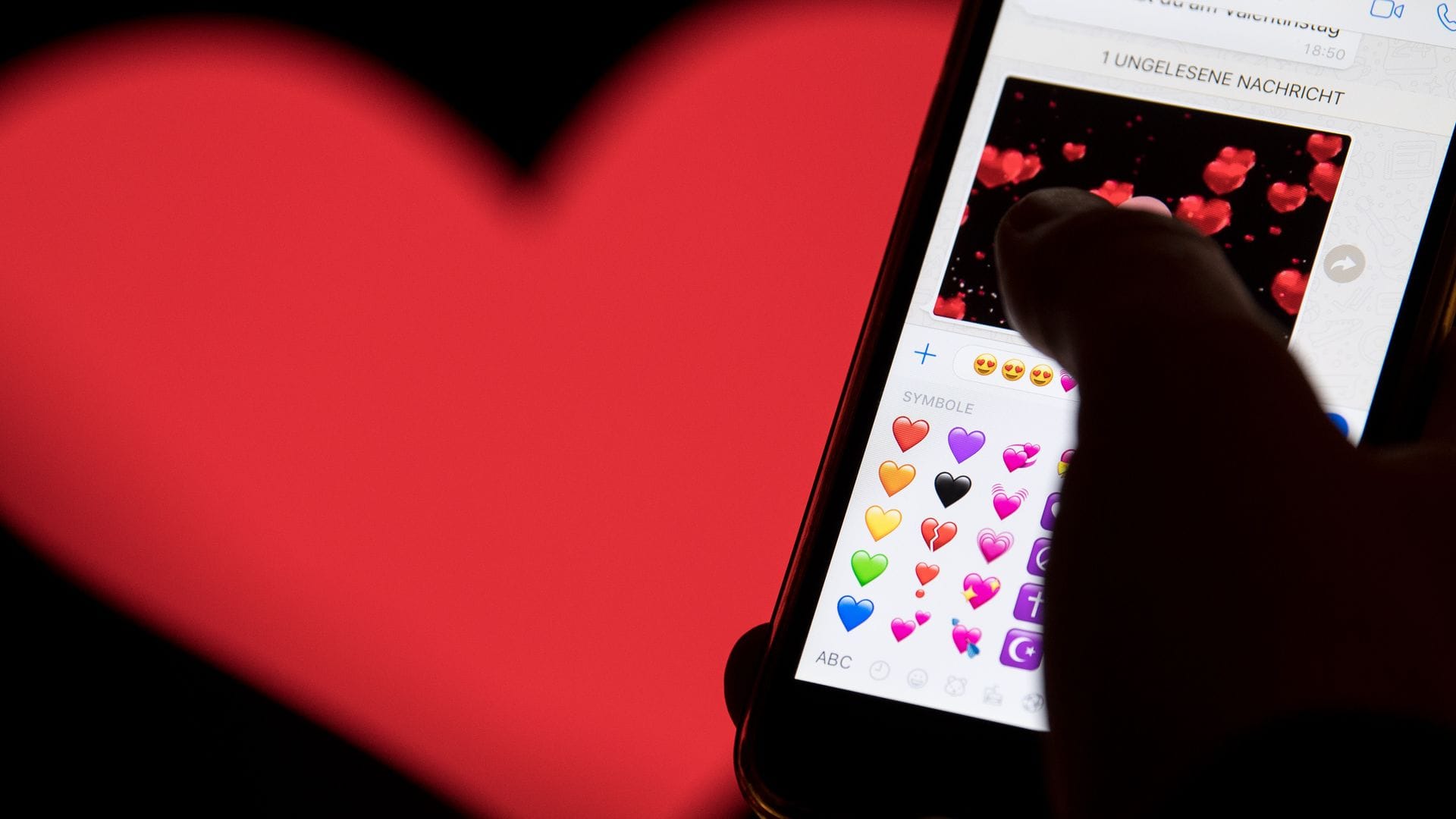 Hand aufs Handy - das rote Herz zählt zu den beliebtesten Emojis. (Archivbild)