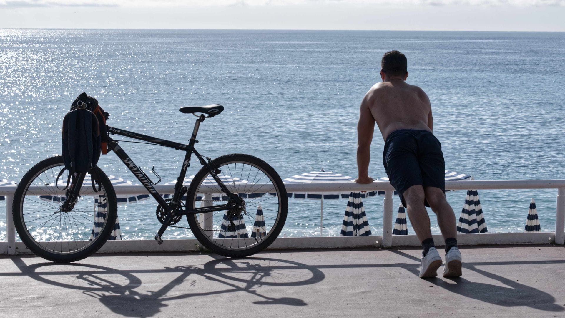 Ein Mann mit nacktem Oberkörper macht am Strand von Nizza neben seinem Fahrrad Übungen. (Archivbild)