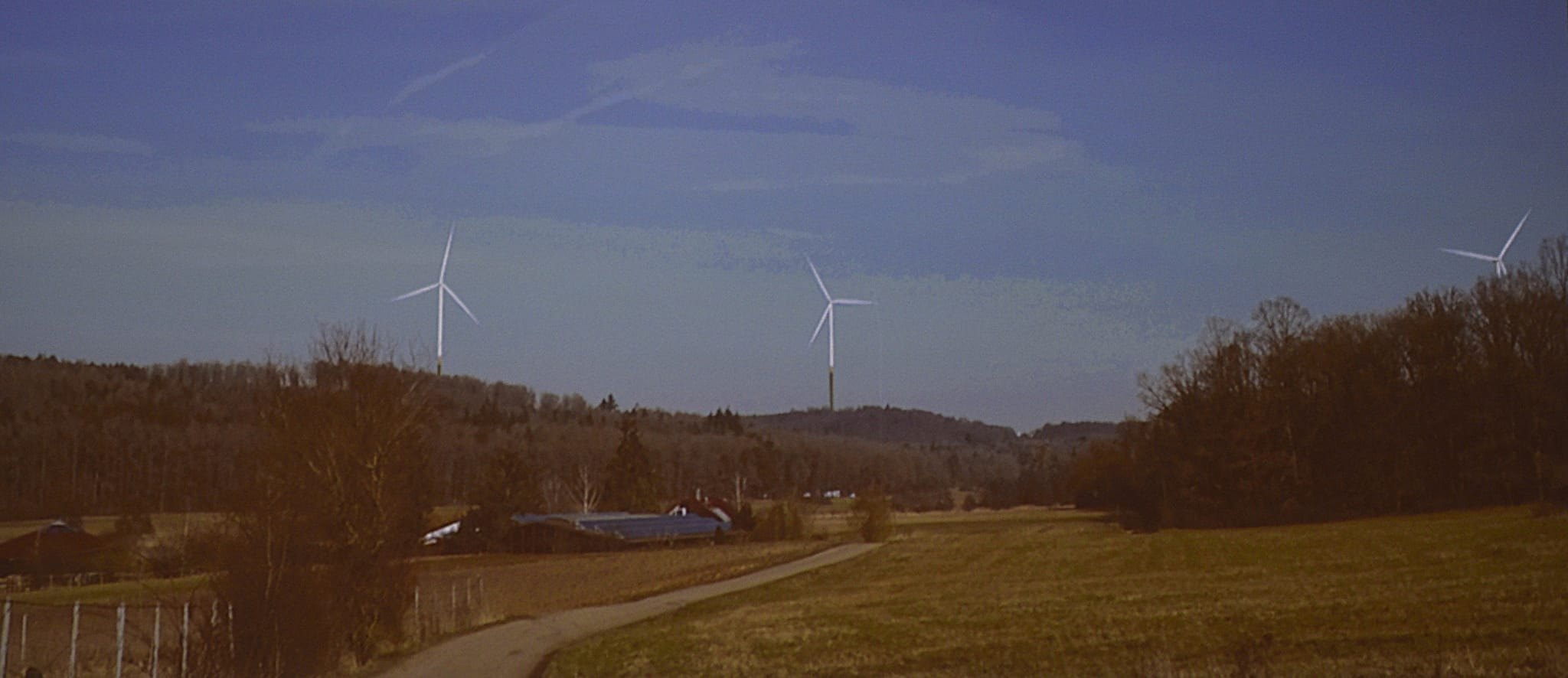 Die beiden Magstadter (links und Mitte) sowie eines der Sindelfinger Windräder (rechts) vom Magstadter Lachenweg aus gesehen. Der Lachenweg, ein Feldweg, beginnt am Kreisverkehr unterhalb des Sportgeländes an den Buchen, ist Teil der Querfeldeinstrecke und wird dann zwischen den Wiesen des Hölzertals und dem unteren Waldrand der Winterhalde weiter in Richtung Osten geführt.