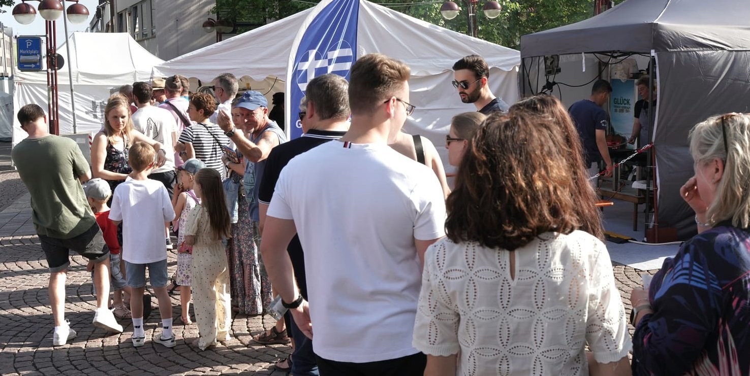 Schon fast obligatorisch ist die lange Warteschlange vor dem Stand der Griechen.