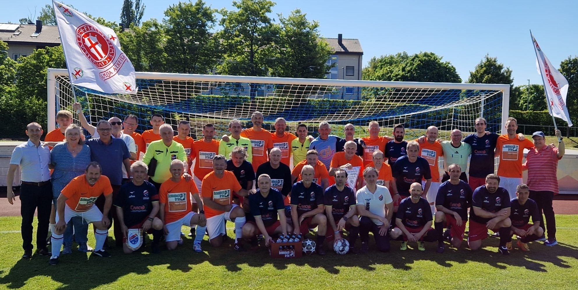 Die Teams vor dem Anpfiff mit OB Dr. Stefan Belz, Uschi Russell, Massimo Lampugnani, Domenico Boeri (von links ohne Trikot) und Carmelo Franchesini (links im gelben Schiedsrichterdress), sowie Ron Russell (ganz rechts). Das Team der Kanne-Knobler (orange Trikots): Vincent Fleck, Team-Manager Thomas Schulz, Alexander Popov, Vladimir Harachasch, Vitaly Kurkov, Ralf Allgöwer, Thomas Fritz, Martin Oßwald, Karsten Zink, Frank Sieber (hinten von links), Lothar Wanner, Axel Arndt, Fabian Rau, Torwart Peter Böttinger, Steffen Müller, Karl Ruthardt und Dieter Wünsch (vorne von links). Auf dem Bild fehlt Trainer Josef Stegemann.