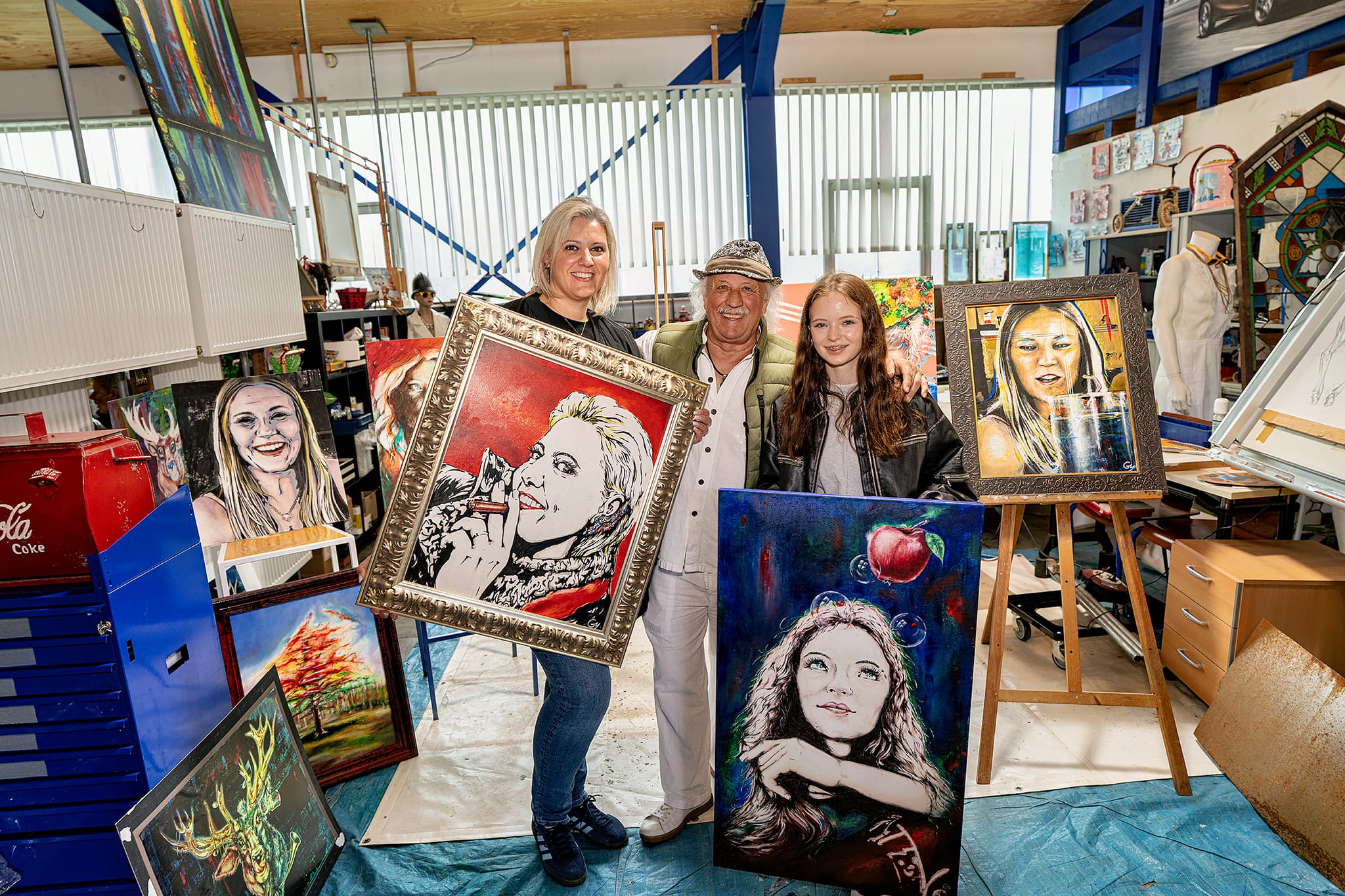 Künstler Georg Müller mit zwei seiner Modelle, die er gemalt hat und die stolz ihre Bilder zeigen. Links Marija Miletic und rechts Laura Schäfer.