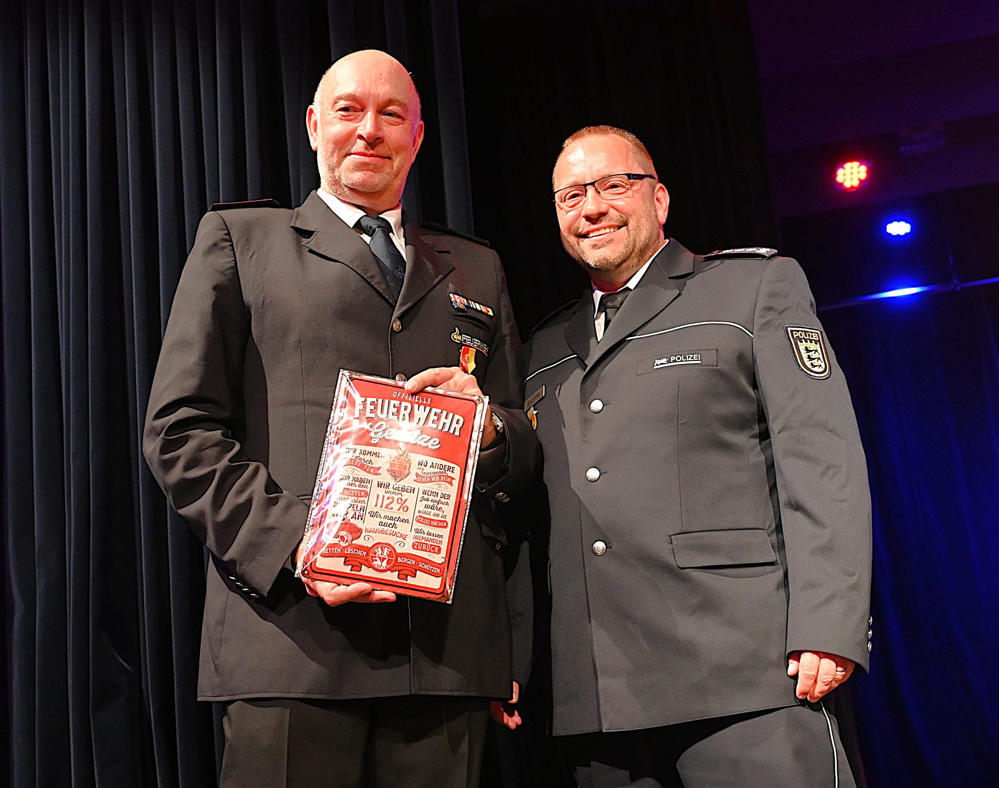 Der langjährige Leiter des Maichinger Polizeipostens, Frank Bechtle (rechts) überreichte Sascha Luft im Namen aller Blaulichtfraktionen die nicht ganz ernst zu nehmenden Feuerwehrgesetze.