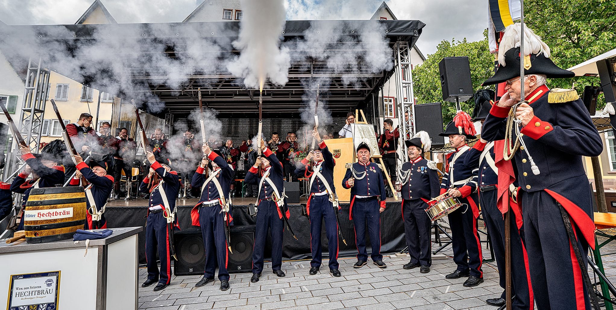 Drei Schuss aus dem Gewehr als Salut zum Stadtjubiläum in Weil der Stadt. Rechts Bürgerwehr-Kommandeur Hartmut Sigel. Bürgermeister Christian Walter am Rednerpult hält sich die Ohren zu. Dahinter der Fanfarenzug.