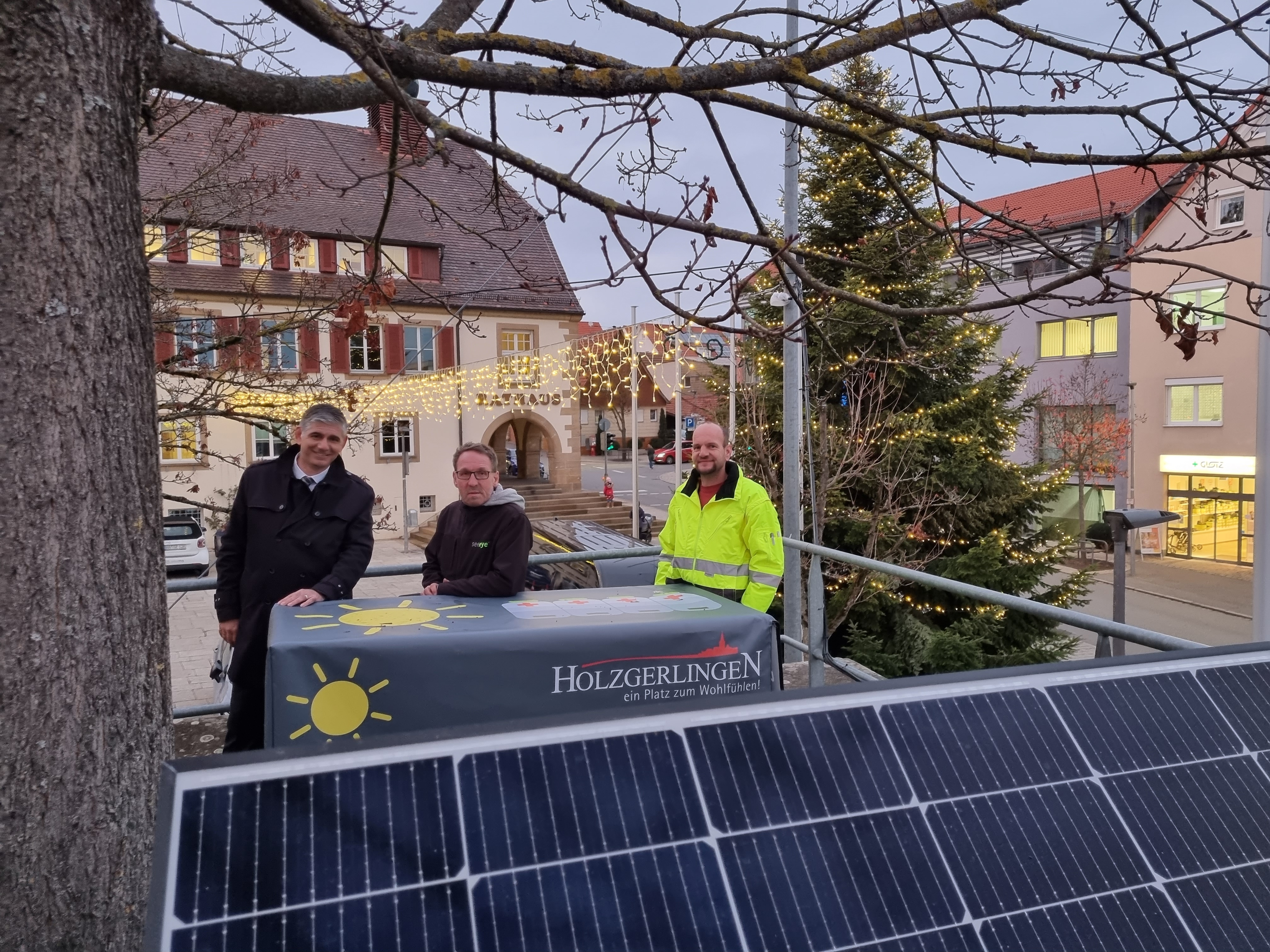 Holzgerlingens Bürgermeister Ioannis Delakos (von links), Seeeye-Geschäftsführer Rüdiger Schmidt und Stadt-Elektriker Volker Krauß vor dem leuchteten Weihnachtsbaum auf Rathausplatz. Eine auf dem Kirchplatz installierte PV-Anlage liefert in den kommenden Wochen den Strom für den Lichterglanz.     Bild: Hamann