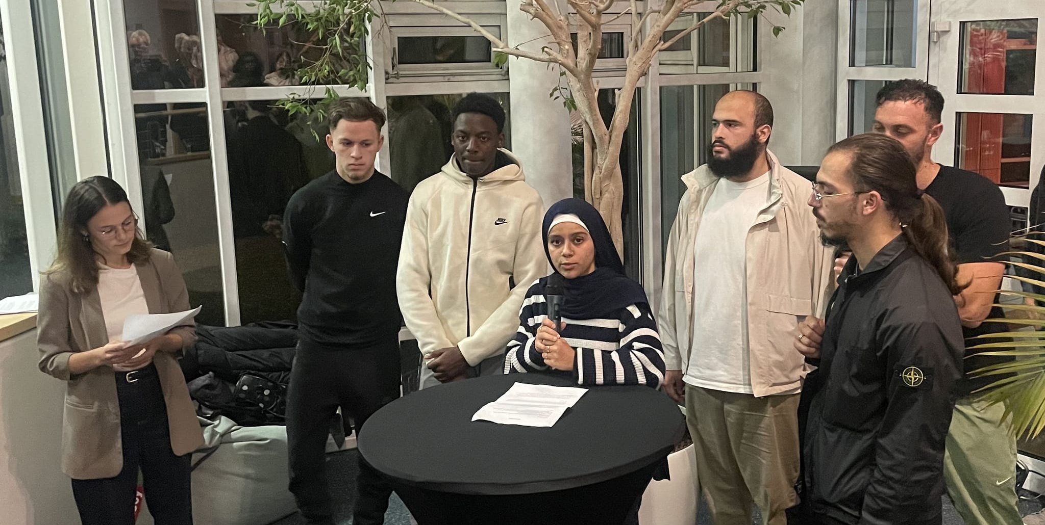Sariya Chalabi am Rednerpult bei der Vernissage für die Fotoausstellung in der Sindelfinger Musikschule mit ihren Kollegen Samy Gallouze, Yakob Saidani, Alhasseynon Drame, Bilal Bourlier, Betreuer Kalil Alessi und Fabienne Schimek (ganz links).