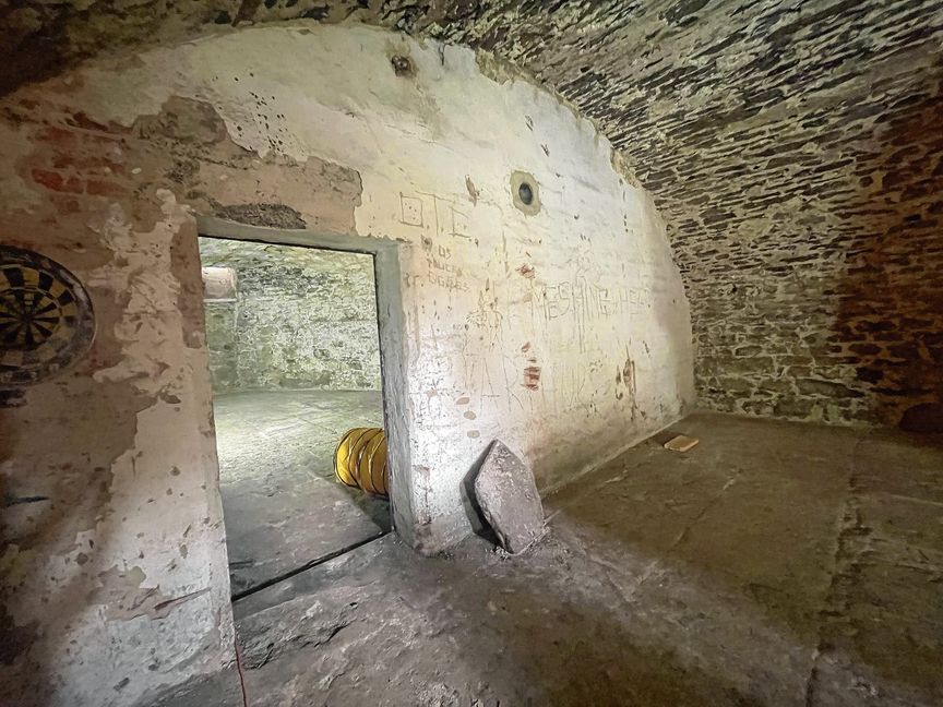 Der erste Keller: Die Mauer mit der Tür stammt aus den 30er Jahren. Die Dartscheibe und die Kritzeleien an der Wand sind allerdings nicht so alt: Wahrscheinlich stammen sie von Jugendlichen aus den 80er oder 90er Jahren, sagt Thomas Banholzer. Sie haben hier wohl gut gefeiert, wie auch unzählige Bierflaschen belegen.