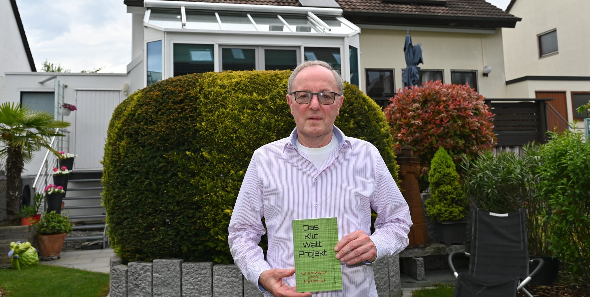 Manfred Maurer mit seinem Taschenbuch über die eigene Energiewende. Im Hintergrund die Doppelhaushälfte mit der PV-Anlage. Solarpaneele wurden natürlich auf der Südseite, aber auch auf der Nordseite und auf dem Garagendach installiert