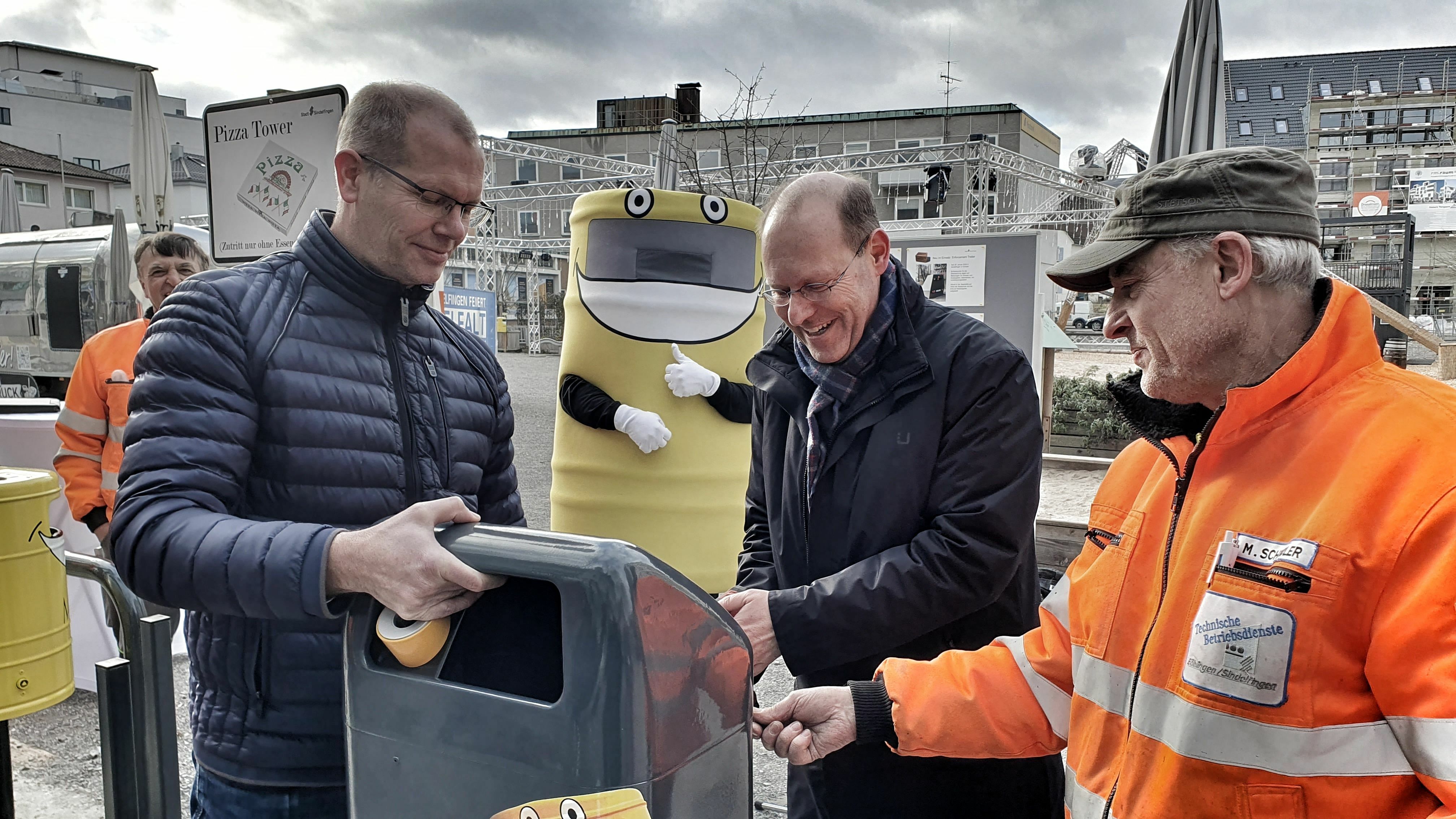 Grünamt-Leiter Ralf Bültge-Bohla, Oberbürgermeister Dr. Bernd Vöhringer und Martin Schindler von den Technischen Betriebsdiensten bringen den ersten Mülltoni 2.0 am Grünen Platz an (von links).     Bild: Wegner